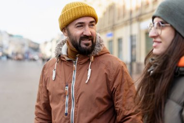 İki turist, hareketli bir şehir caddesinde kış yürüyüşünün keyfini çıkarırken, canlı sohbetler yapıyorlar ve çevrelerindeki canlı kentsel manzarayı keşfediyorlar.