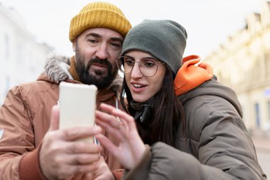 Kışlık giysiler giymiş sakallı adam ve genç kadın soğuk bir kış günü şehri keşfederken seyrüsefer için akıllı telefon uygulaması kullanarak birlikte şehir maceralarının tadını çıkarıyorlar.