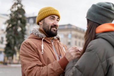 Bereli ve kışlık paltolu sakallı bir adam serin bir kış günü açık havada hassas bir anı paylaşırken arkadaşının elini nazikçe tutar.