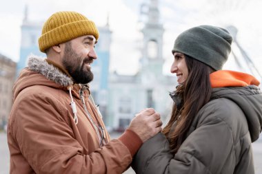 Kış kıyafetleri ve rahat taksiler giyen mutlu çift, el ele tutuşup gülümserken bulutlu bir kış gününün tadını çıkarıyorlar.