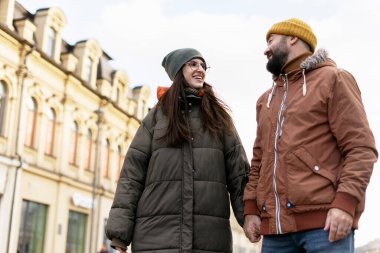 Serin bir kış günü şehirde sakin bir şekilde yürürken el ele tutuşan neşeli genç çift birlikte keşfederken sevgi ve şefkat saçıyorlar.