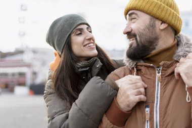 Neşeli çift dışarıda romantik bir anın tadını çıkarırken, kadın erkeği kucaklarken, birbirlerine gülümserken, ikisi de kalın kışlık elbiseler ve taksiler giyiyorlar.