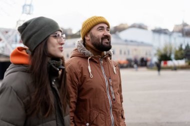 Sıcak kışlık giysiler giymiş mutlu çift bulutlu bir sonbahar gününde şehri geziyor, gülümsemelerini ve beraberliklerini paylaşıyorlar.