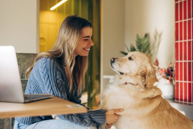 Genç bir kadın dizüstü bilgisayarına ara veriyor. Sıcak, modern dairesinde köpeğini sevgiyle okşuyor. Sıcak bir bağ ve rahatlama ortamı yaratıyor.