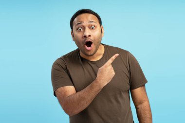Şaşırmış bir adam parmağını mavi arka plandaki kopyalama alanına doğrultuyor. Ağzı şaşırtıcı bir şekilde açık. Heyecan verici ya da inanılmaz bir şeyi işaret ediyor.
