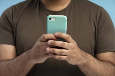 Elinde açık mavi bir akıllı telefon tutan bir adamın dijital çağda iletişim ve bağlantı kurmak için mobil teknolojiyi kullanması.