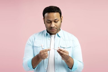 Odaklanmış adam elinde bir mızrak ve glukometre tutuyor. Kan şekeri seviyesini ölçmeye hazırlanıyor. Bu da canlı, pembe bir arka plana karşı sorumlu diyabet yönetimini gösteriyor.