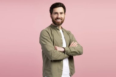 Stüdyoda pembe bir arka planda kollarını kavuşturmuş gülümseyen Latin bir adamın portresi. Alışveriş, reklam konsepti.