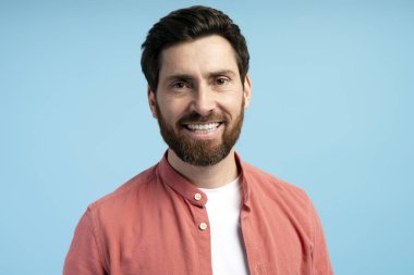 Mavi arka planda izole edilmiş, sıradan gömlekli mutlu sakallı bir gencin portresi. Alışveriş, reklam konsepti.