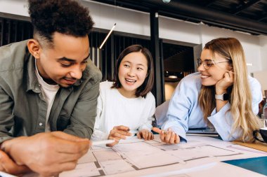 Üç farklı mimar modern bir ofisin planlarını inceliyor, gülümsüyor ve ev planlarını tartışıyor, takım çalışması ve işbirliği gösteriyor. Takım çalışması konsepti