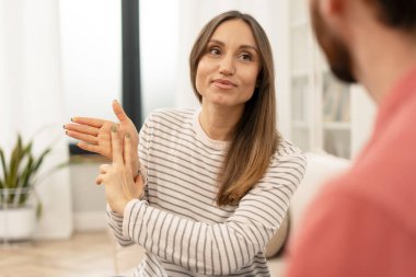Parlak, rahat bir ofiste terapisti ile iletişim kurarken işaret dili kullanan genç bir kadın, zihinsel sağlık desteğinde anlayış ve bağlantıyı teşvik ediyor.