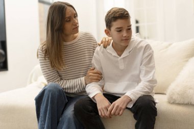 Depresyondaki oğlunu destekleyen, evdeki kanepede yan yana otururken onu teselli eden, teselli eden, ebeveyn desteği ve aile anlayışı kavramını önemseyen anne.