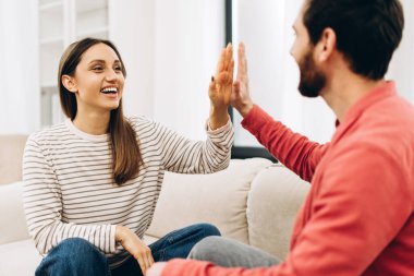 Mutlu çift evde rahat bir koltukta oturup beşlik çakıyor, başarılı bir projeyi veya harika bir haberi kutluyor, birlikte vakit geçiriyorlar.