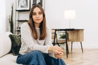 Modern, şık bir oturma odasında rahat bir koltukta oturan genç kadın derin düşüncelere dalmış, elleri nazikçe kucağına yapışmış, sakin bir iç gözlem anının tadını çıkarıyordu.