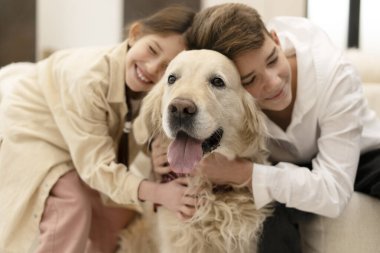 Erkek ve kız kardeşler, sevimli Golden Retriever köpeklerine sarılıp kucaklaşıyorlar. Tüylü aile üyelerine sevgi ve şefkat gösteriyorlar.