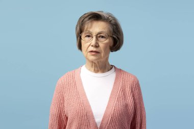 Mavi arka planda gözlük ve pembe hırka giyen son sınıf öğrencisi ciddi bir kadının portresi.