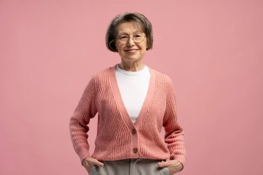 Pembe bir arka planda kendine güvenen ve mutlu görünen son sınıf bir kadının stüdyo portresi.