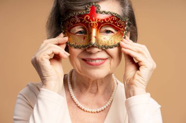 Kırmızı ve altın rengi Venedik karnaval maskesi takıp Mardi Gras partisine hazırlanan inci kolyeli son sınıf öğrencisi.