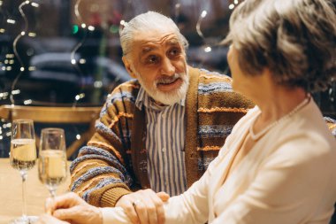 Sıcak bir restoran masasında oturan yaşlı bir çift sıcak bir sohbete girişiyor. Yumuşak ışıklandırma samimi bir atmosfer yaratır, şampanya bardakları da bir parça kutlama katar. Randevu konsepti
