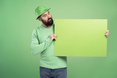Yeşil St. Patrick Günü şapkalı bir adam yeşil arka plandaki boş yeşil tabelayı işaret ediyor.