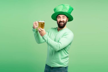 Yeşil Aziz Patrick Günü şapkalı sakallı adam yeşil arka planda bir bardak birayla kadeh kaldırıyor.