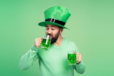 Yeşil cüce şapkalı, yeşil bira içen sakallı adam yeşil arka planda Aziz Patrick gününü kutluyor.