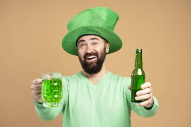 Sakallı, yeşil cüce şapkalı, şişe ve bir bardak yeşil bira sunan mutlu adam Aziz Patrick gününü kutluyor.