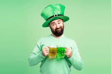 Yeşil St. Patrick şapkalı sakallı adam, iki kupa tutuyor, biri yeşil biralı, diğeri de bira biralı, Aziz Patrick Günü 'nü kutluyor.