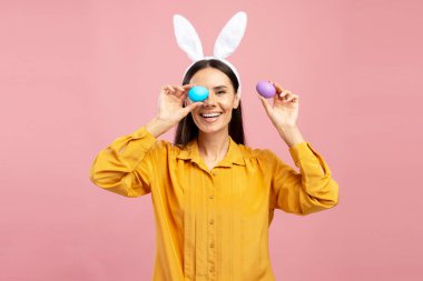 Renkli paskalya yumurtaları tutan, tavşan kulaklığı takan, Paskalya bayramını kutlayan neşeli bir kadının stüdyo portresi.