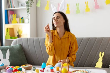 Paskalya yumurtalarını evde boyayan, tavşan kulaklığı takan, renkli yumurta kokan ve paskalya geleneklerinin tadını çıkaran bir kadın.