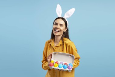 Tavşan kulaklı neşeli kadın elinde renkli paskalya yumurtaları, gülümseyerek Paskalya bayramını kutluyor.