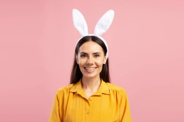 Tavşan kulağı takan gülümseyen kadının stüdyo portresi pembe arka planda Paskalya kutlaması.