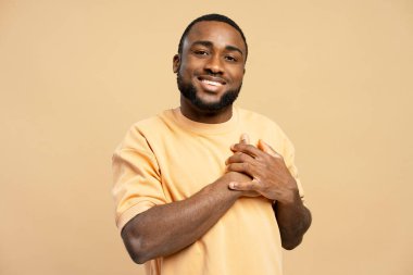 Minnettar Afrikalı Amerikalı adam elleri göğsünde gülümsüyor. Yumuşak bir bej arka plana sıcaklık ve pozitiflik yayıyor.
