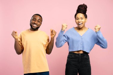 Mutlu bir adam ve kadın zaferi kutluyorlar. Havaya atılan yumruklarla. Heyecan ve neşeyi canlı pembe arka planda ifade ediyorlar.