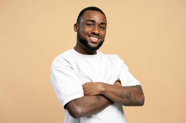 Kollarını kavuşturup gülümseyen, kendine güveni ve pozitifliği olan Afro-Amerikan bir adamın stüdyo portresi.