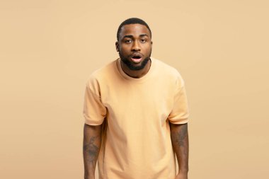 Şaşırmış genç bir adamın stüdyo portresi. Bej arka planda sıradan bir tişört giyiyor.