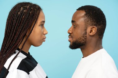 Mavi arka planda birbirlerine bakan Afrikalı ciddi bir çiftin yan görünüm portresi.