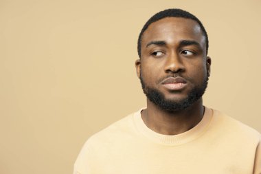 Sakallı, düşünceli bir gencin stüdyo portresi. Tarafsız bir bej arka planda duygularını ifade ediyor.