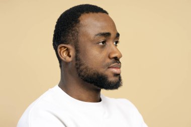 Bej bir arka planda poz verirken sakallı, ciddi bir Afrikalı Amerikalı adamın profili.