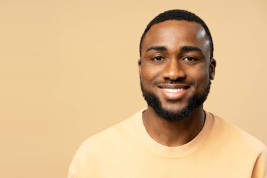Bej bir arka planda gülümseyen, mutluluk ve pozitifliği ifade eden neşeli, Afro-Amerikan bir adamın portresi.