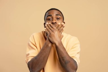 Stüdyo portresi, elleri yumuşak bej bir arka plan karşısında ağzını kapayan genç bir adamın sessizlik ve tefekkür duygusunu aktardığı.