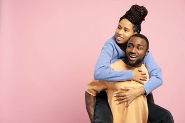 Genç Afrikalı Amerikalı kadın erkek arkadaşını kucaklıyor ve pembe arka planda izole bir şekilde eğleniyor.