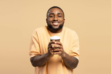 Neşeli, Afro-Amerikalı bir adam. Kahvesini yudumluyor, gülümsüyor ve elinde bej bir arka planda kağıt bardak tutuyor.