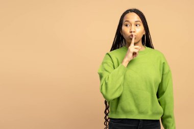 Yeşil süveter giyen genç bir kadın bej arka planda sessizce hareketler yapıyor.