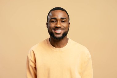 Gülümseyen Afrikalı genç Amerikalı adamın bej arka planda poz veren günlük bej kazak giymiş portresi