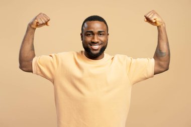 Neşeli bir Afrikalı Amerikalı 'nın portresi gücünü gösteriyor ve bej bir arka planda gülümsüyor.