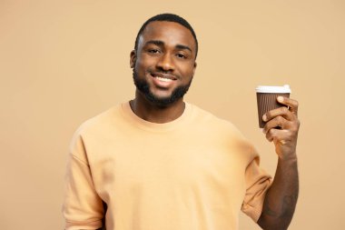Stüdyoda gülümseyen ve bej arka planda tek kullanımlık kahve fincanı gösteren siyah bir adam.