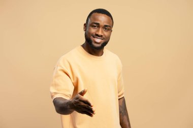 Gülümseyen ve el sıkışmak için elini uzatan genç bir yetişkin. Tarafsız bir arka plan için dostluk ve isteklilik gösteriyor.