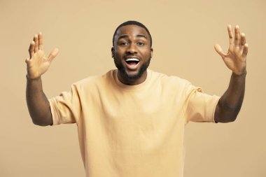 Heyecanlı Afrikalı Amerikalı genç adam elini kaldırıyor ve bej arka planda gerçek bir sürpriz gösteriyor.