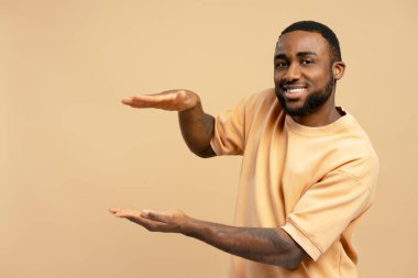 Elleriyle hareket eden genç bir adamın stüdyo portresi. Sanki bej bir arka plana gülümseyen bir şeyin boyutunu gösteriyor gibi.